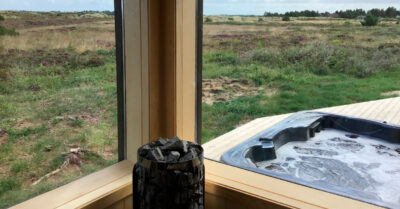 Udsigt fra sauna til spa og den jyske hede. Saunaen har stort panoramavindue, der lader saunagæster interagere med gæster i spaen|Udespa sauna udsigt. Begge er placeret på terrassen med flot view ud over den jyske hede. Saunaen har et stort panoramavindue.|Saunahus og udespa med udsigt over den jyske hede. Flot lyst asketræ i saunarummet og comfortana Pro udespa beregnet til udlejningshus.|Lækker indrettet sommerhusafdeling med sauna og spa med panorama view ud over den jyske hede|Saunaplads med udsigt. Nybygget sauna i forbindelse med udendørs spa. Store panoramavinduer giver kig ud over den jyske hede.|Udendørs spabad ved sauna. Begge har flot udsigt ud over den jyske hede. Sauna har kig gennem panoramavinduer.|Panoramavindue ved sauna med indsigt til det smukke lyse asketræ og udsigt til den store jyske hede. Saunaovn fra Harvia.