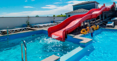 Rutsjebane hos Grønninghoved Camping, hvor der er installeret nye effektive varmepumper til opvarmning af pladsens bassiner.|Wellness by DuoLine logoplade placeret på de store nye Luft til vand varmepumper for swimmingpools hos Grønninghoved Camping.|Luftvand varmepumper er skiftet hos Grønninghoved Strand Camping
