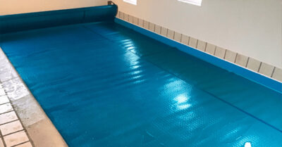 Termotæppe på swimmingpool. Det effektive og slidstærke Geobubble termotæppe har dobbelt boble og lang levetid. Holder fordampningen inde.|Foliepool i howaii - før folien skiftes. Den gamle folie har mistet pusten og har lsuppet taget i bagbeklædningen.|Så står bassinet uden folie.|Indstøbningsdele skal der også tages hensyn til ved udskiftning af folie. Her er lampe og dyser ny monteret og folien monteres, så der undgås utætheder.|Foliemontering ved pool stige i indendørs swimmingpool|Pool liner under opsætning i feriehus. Foliemontering i indendørs swimmingpool. Farve blå.|Termotæppe oprul. Tæppet er tilskåret, så det passer til bassinets udformning. Geo bubble termotæppe er af høj kvalitet og med lang levetid.|Swimmingpool med vand efter at pool lineren er blevet skiftet. Vandet har et grønt skær indtil det har været igennem klordosering.